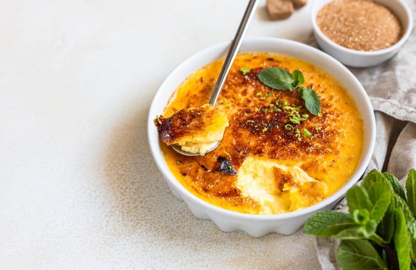 A golden crab brûlée served in a ramekin with a caramelized top and fresh herbs.